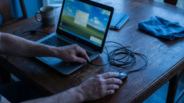 Hands connect a laptop charger and position a mouse while preparing a Windows computer for BlueStacks installation.