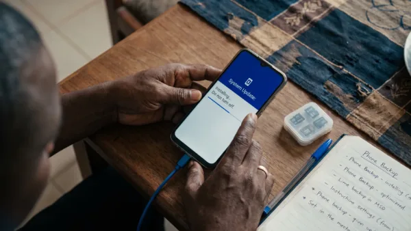 Hands prepare a phone update on a dining table with charging gear and backup storage nearby.